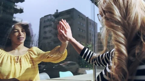 Video of two friends touching her hands separated by a glass window for socia Stock Footage 152988845