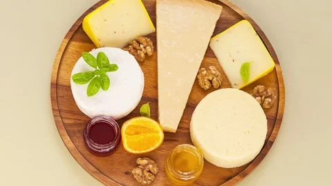 Video of various types of cheeses with basil, honey, fruit jam on wooden plate Stock Footage 305444111