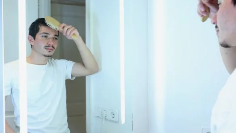 Video of young man combing his hair with a wooden comb after taking a shower Stock Footage 297666093