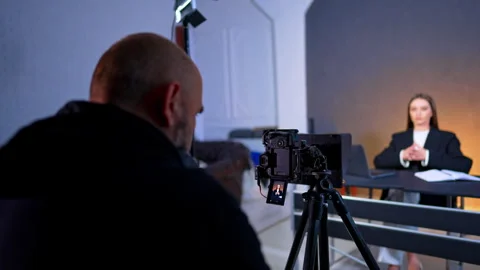 Videographer adjusting camera settings on tripod for studio interview. Over the Vidéo 334812939