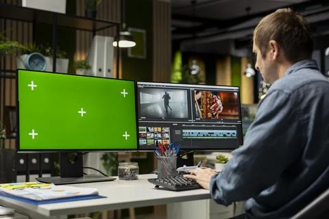 Videographer expert cutting and editing video footage next to green screen Stock Photos