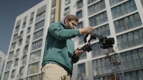 Videographer operator with professional digital camera shoots video on territory Stock Footage 244490632