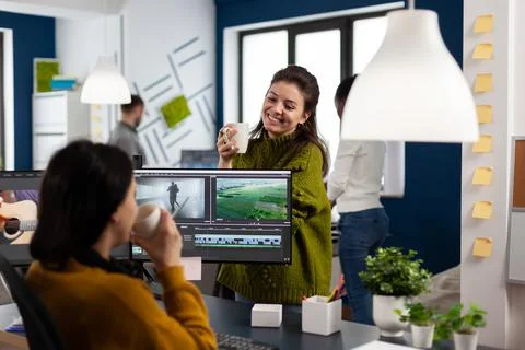 Videographers drinking coffee and talking during work break sitting at desk Stock Photos