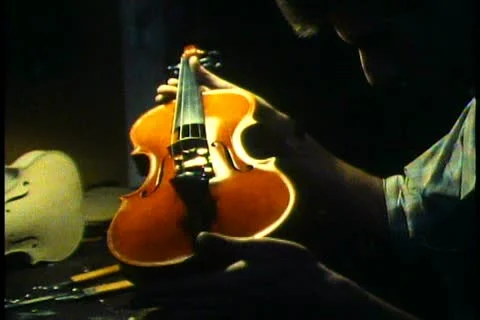 VIENNA, AUSTRIA, 1988, String instrument manufacturing, man examines violin Stock Footage 10920347