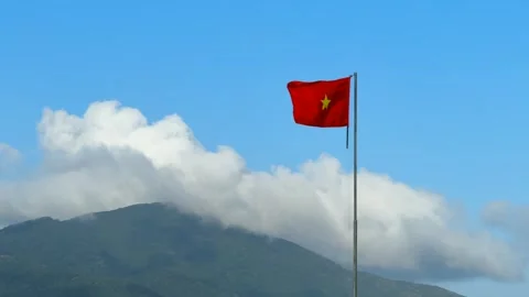 Vietnamese Flag on Tall Pole with Mountain Landscape covered in clouds 库存影片 339045697