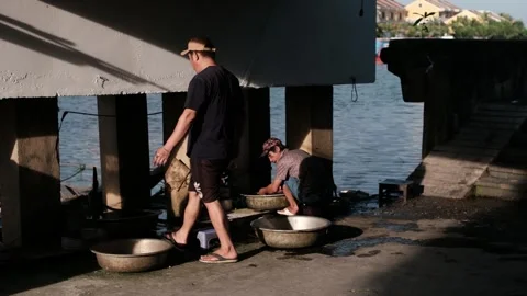 Vietnamese Man Walking by a Riverfront Workspace Under a Concrete Bridge Vidéo 336384919