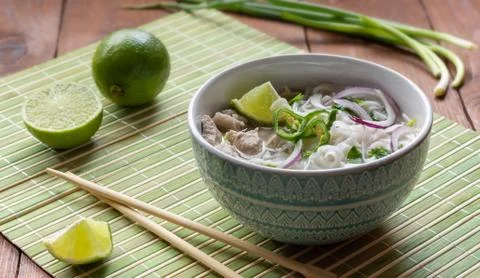 Vietnamese Pho Bo soup with rice noodles and bamboo sticks on a green Mat. Stock Photos