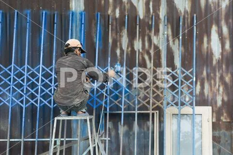 Vietnamese worker painting a fence in Blue Stock Photos