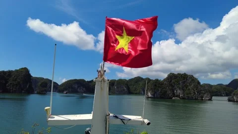 Vietnam's red flag with a yellow star flutters in the wind as a luxury cruise sh Vidéo 329056328