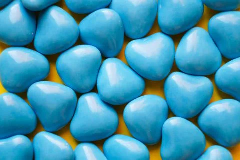View from above. Blue dragee in the shape of hearts on a yellow background. Stock Photos
