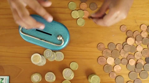 View from above of a boy saving money, putting coins in the metal bank. Savin Stock Footage 135968015