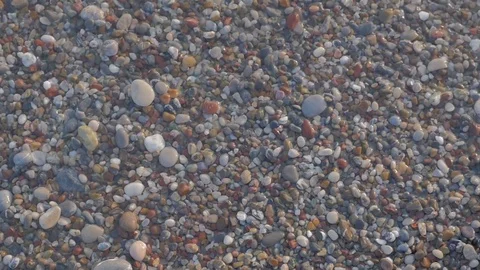 A view from above of waves, foam and colored stones. Pebble beach Video stock 80669043