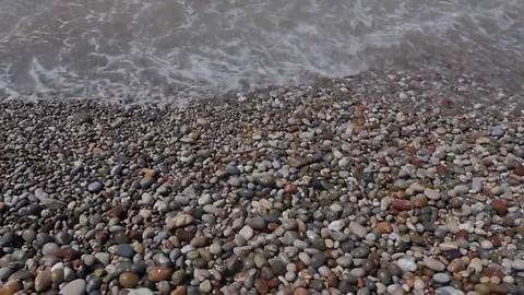 A view from above of waves, foam and colored stones. Pebble beach Stock Footage 81691737