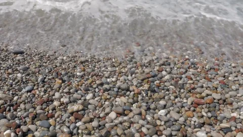 A view from above of waves, foam and colored stones. Pebble beach Stock-Footage 81692946