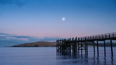 View across calm lapping water in Hokianga Harbour at dawn with full moon Vídeo Stock 92615740