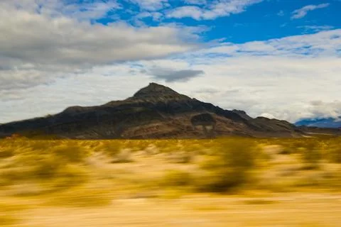 View across a desert landscape to a sharp peak, seen from a moving vehicle. Stock Photos