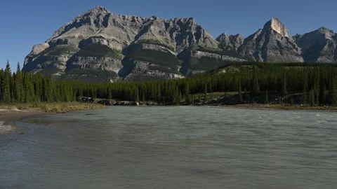 View Across a Fast Flowing Park River with Rocky Mountains and Clear Blue Sky in Stock Footage 331683914
