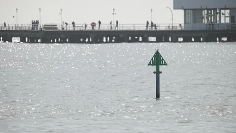 View across a sparkling sea to distant silhouettes of people on a pier 4K tripod Stock Footage 219780010