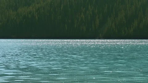 View across a turquoise colored mountain lake with the summer sky flashing on Stock Footage 340240190
