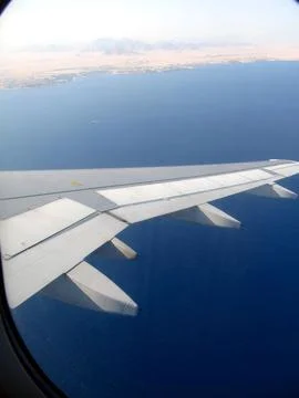 View From the Airplane Porthole Showcasing the Wing Over a Vast Blue Ocean .. Stock Photos
