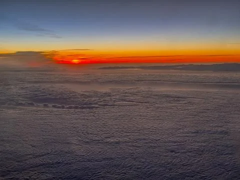A view from an airplane of the sun setting behind the clouds. Stock Photos
