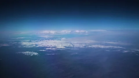 View from airplane window on cloudy blue sky with snow-capped mountains Stock Footage 147939220