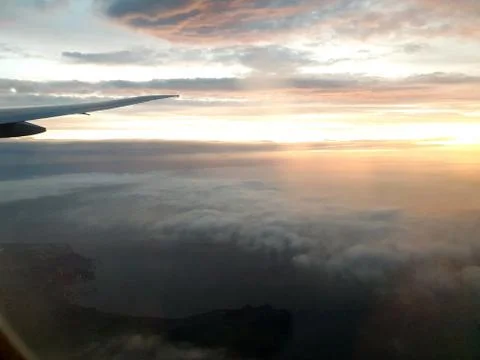 View from airplane window inside the clouds with colorful sunrise Stock Photos