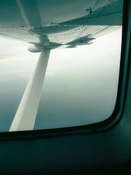 View from airplane window shows wing, engine, and ocean horizon Stock Photos