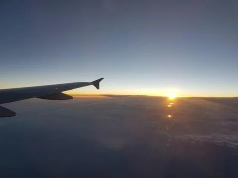View from an airplane window as the sun rises over the horizon, casting golden r Fotos de archivo