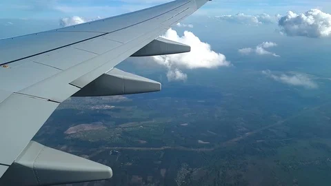 View from the airplane window on the wing, clouds and the ground, flying above Stock Footage 98699111