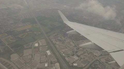 View of Airplane Wing Outside of Window Flying Through Clouds Above City Stock Footage 100837288