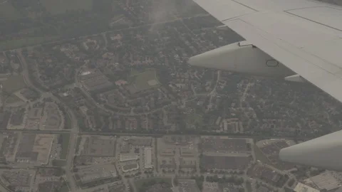 View of Airplane Wing Outside of Window Flying Through Clouds Above City Stock Footage 100837664