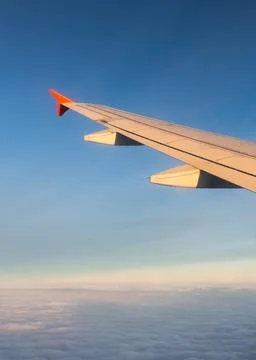 View from airplane wing over clouds at sunset during travel in clear skies Stock Photos
