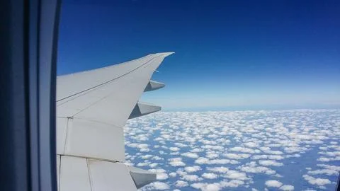 View of an airplane wing from a passenger window during flight above scattered c Stock Photos
