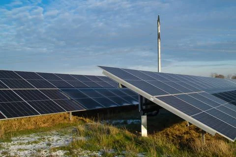 A view of an array of solar panels near a windmill Stock Photos