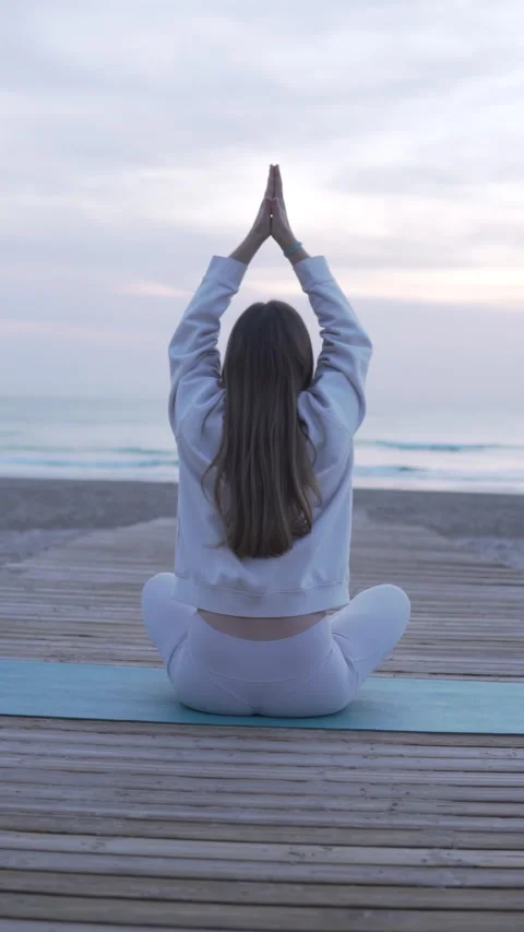 View from the back, brunette woman doing yoga on the beach by the sea Stock Footage 303410291