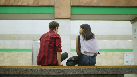 View from the back. A couple is sitting on a bench in the subway and talking. Stock Footage 209629890