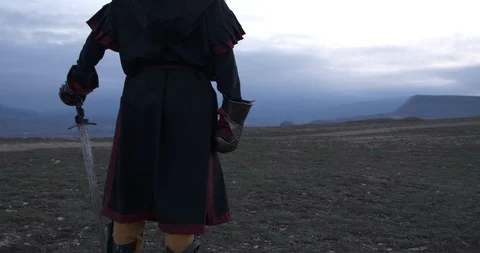 View to the back of knight that stands with sword and looks to horizon Stock Footage 89726940