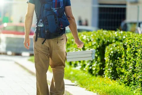 View from the back. A man with a backpack carries three boxes of pizza in the 写真素材