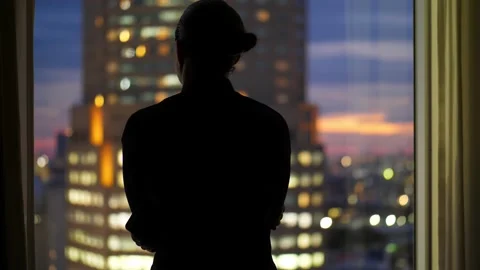 View from back of man silhouette against window, he looks out to evening city Stock Footage 218311387