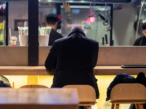 View from the back of a man sitting at the bar in a fast food restaurant. Bus Stock Photos