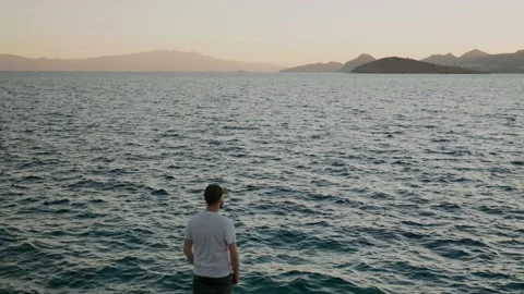 View from the back of a man in a white T-shirt admiring the sea, standing on the Stock Footage 220732825