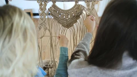 View from the back, two women blonde and brunette weaving macrame Stock Footage 237710168