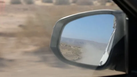View into back view mirror of 4x4 vehicle driving on dry and dusty gravel track  Stock Footage 102733015