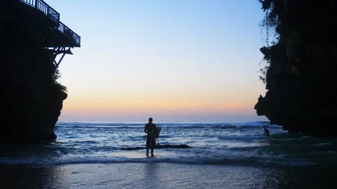 View from the back of a white man standing with a surfboard between two cliffs Stock Footage 105007664