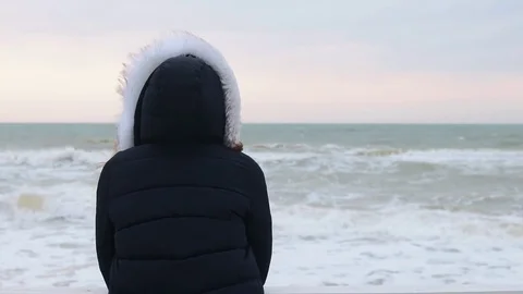 View from the back a woman in a winter jacket with a hood looking at the sea Stockbeeldmateriaal 72191254