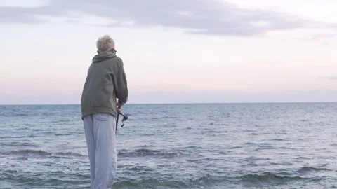 View from the back, young blond guy in sweatshirt and jeans fishing in the sea Stock Footage 322173784