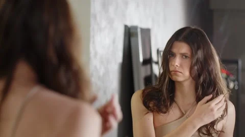 View from the back of a young brunette combing her hair in front of a mirror Video stock 239328233