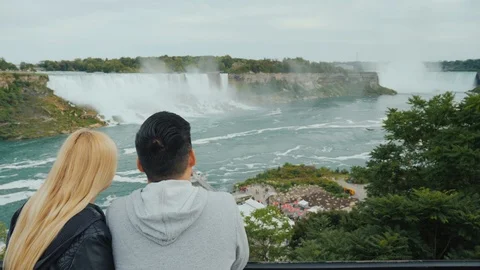 View from the back of a young multi-ethnic couple looking at the famous Niagara Stock Footage 100590626