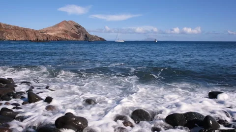 View of beach in Madeira with volcanic pebble shoreline, rolling Atlantic waves Stock Footage 345840986